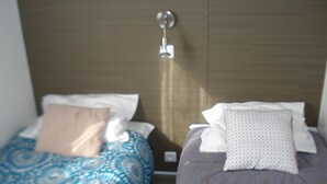 Dos camas con ropa de cama estampada, una lámpara fijada a la pared y un panel de madera.