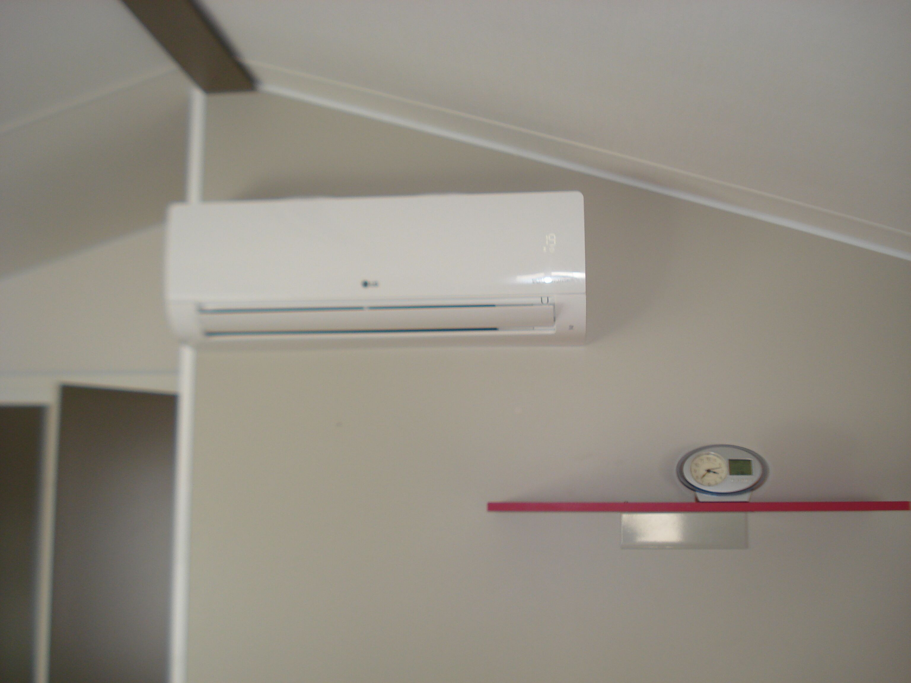 Un climatiseur blanc fixé au mur, une balance et une étagère rouge.