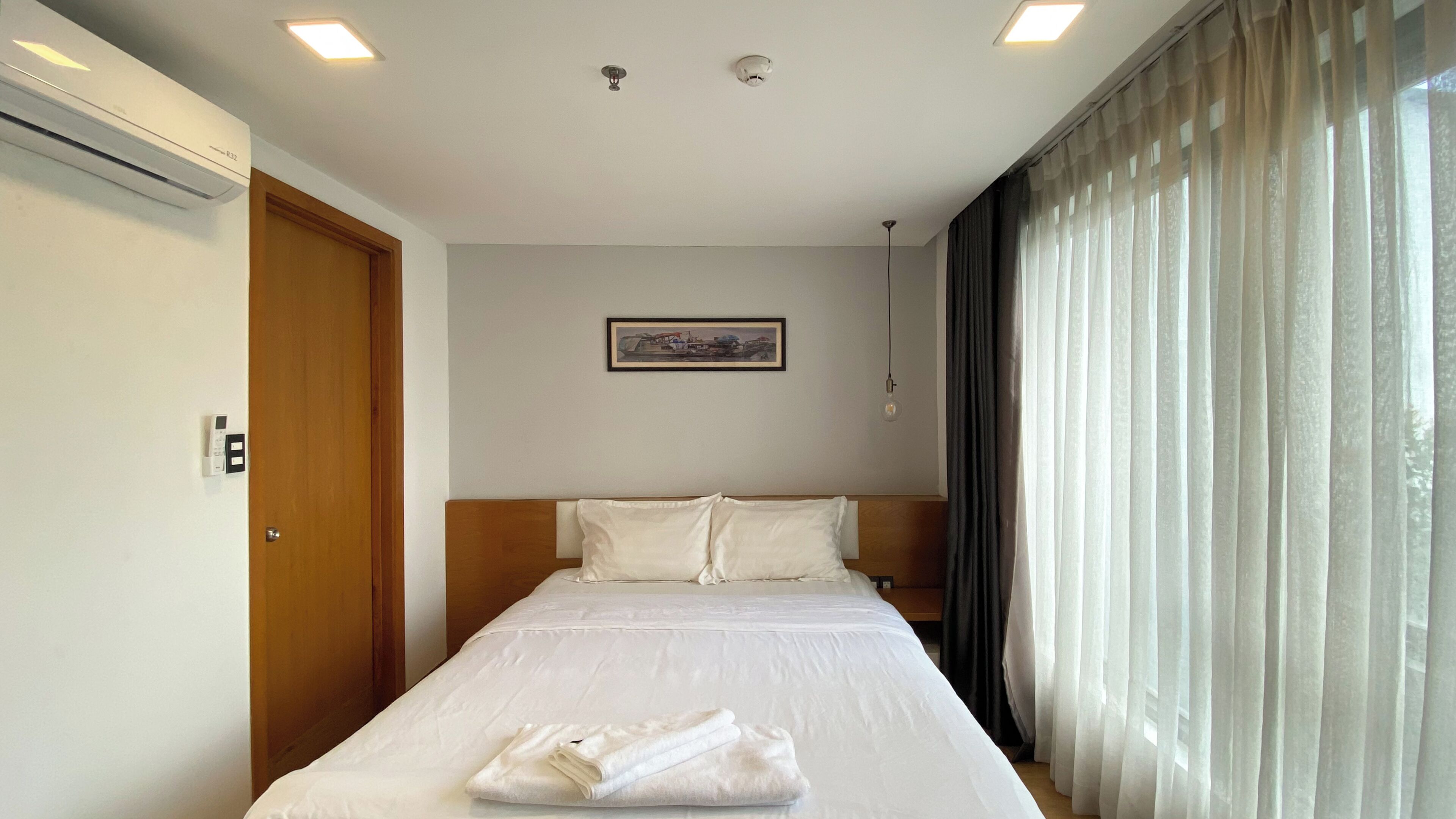 Una habitación de hotel con una cama, un cuadro en la pared y un ventanal con cortinas.