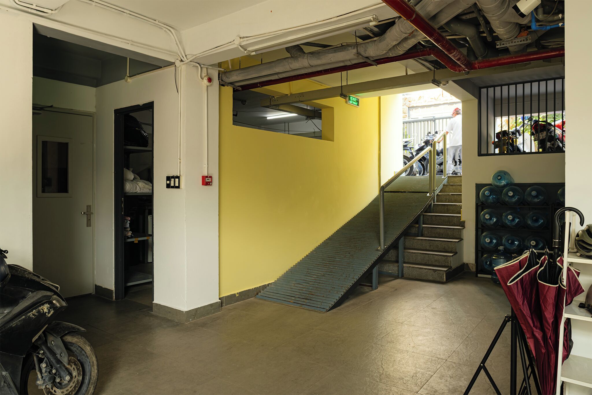 A stairway leading to an upper level, a motorcycle parked to the left, and a rack with umbrellas to the right.