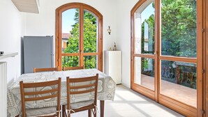 A dining area with a table and chairs, a refrigerator, and large arched windows with a view of greenery. - Casa Del Paperotto (Peschiera del Garda)