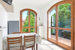 Ein Essbereich mit Tisch und Stühlen, einem Kühlschrank und großen Bogenfenstern mit Blick ins Grüne.