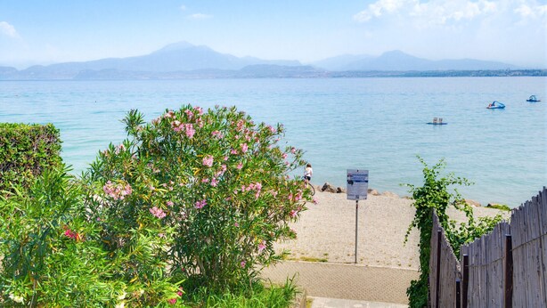 A beach with a clear view of the sea, a mountain in the distance, and a wooden fence. - Casa Del Paperotto (Peschiera del Garda)