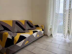 A room with a sofa, a window with sheer curtains, and a tiled floor. - Casa Nina - In downtown Pontedassio, 5 minutes from Imperia, by HOST4U (Pontedassio)