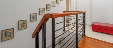 A staircase with a wooden handrail and metal railing, a red bench, and framed pictures on the wall.