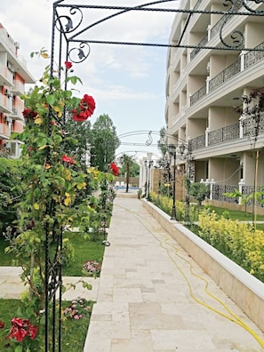 Ein Weg, der von einem Rosengarten und einem Gebäude mit Balkonen gesäumt wird.