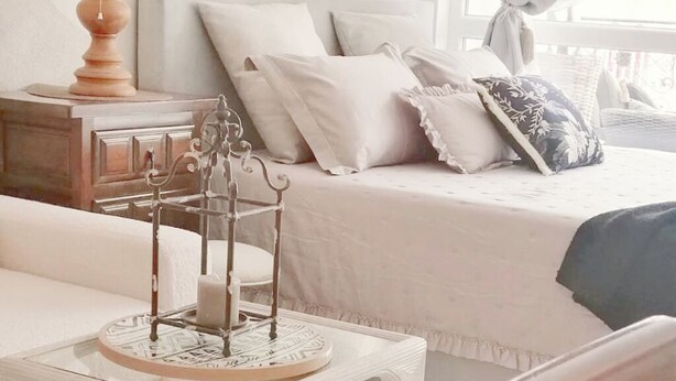 Een slaapkamer met een bed, nachtkastje, lamp en een raam met gordijnen.