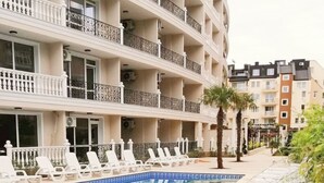 Een hotel met een zwembad, witte ligbedden en een meerlaags gebouw met balkons.