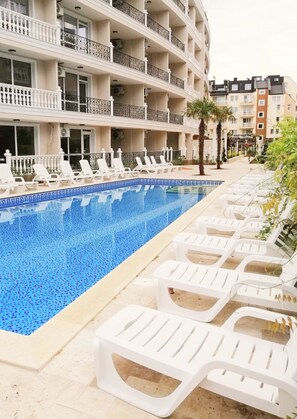Ein Hotel mit Schwimmbad, weißen Liegestühlen und einem mehrstöckigen Gebäude mit Balkonen.