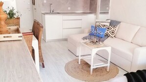 Een moderne woonkamer met een eethoek, een keuken met witte kasten en een witte bank met opvallende kussens.