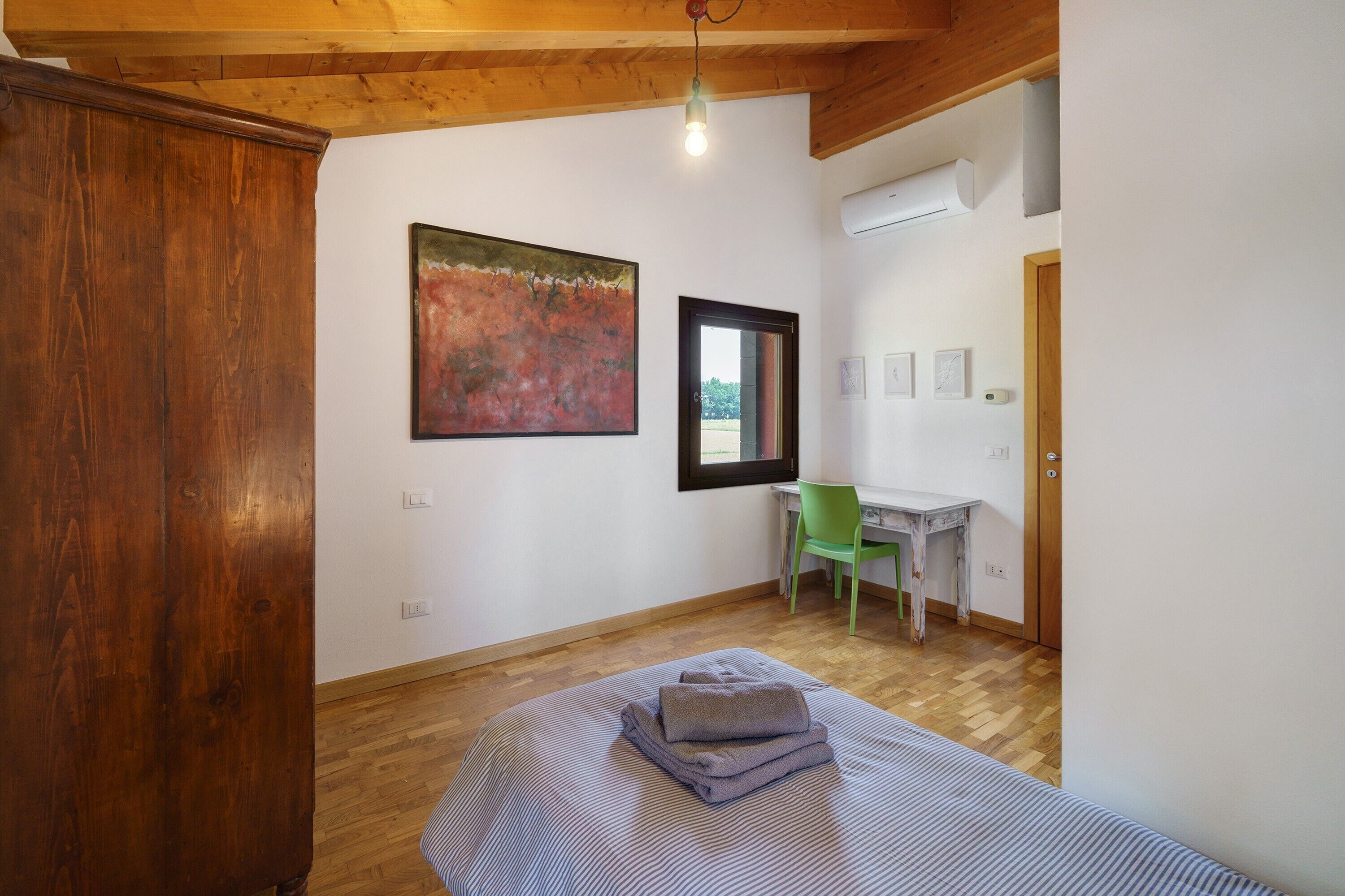A room with a bed, a desk, a chair, a painting, and a wooden cabinet.