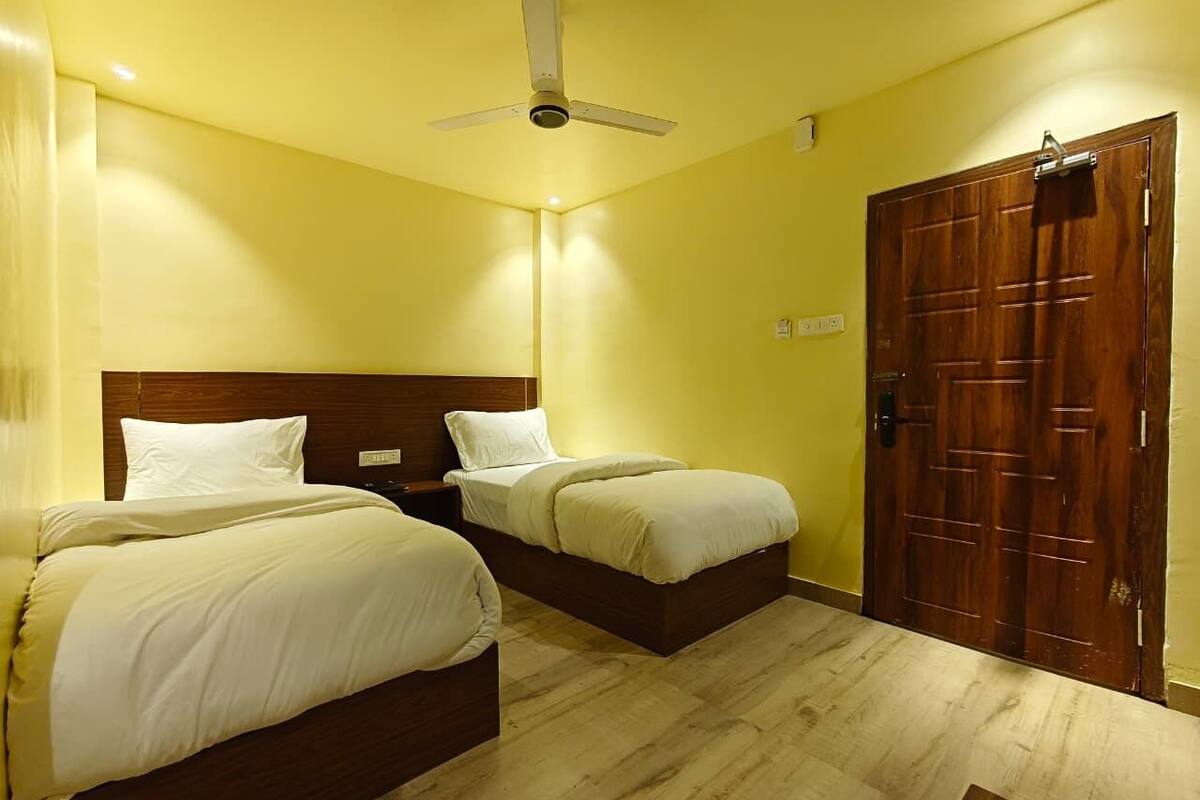 Quarto de hotel com duas camas, uma porta de madeira e um ventilador de teto.
