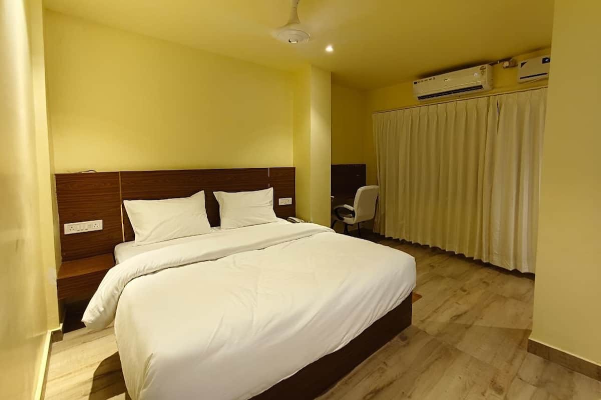 Quarto de hotel com uma cama, um ventilador de teto, ar condicionado, uma cadeira e uma cortina.