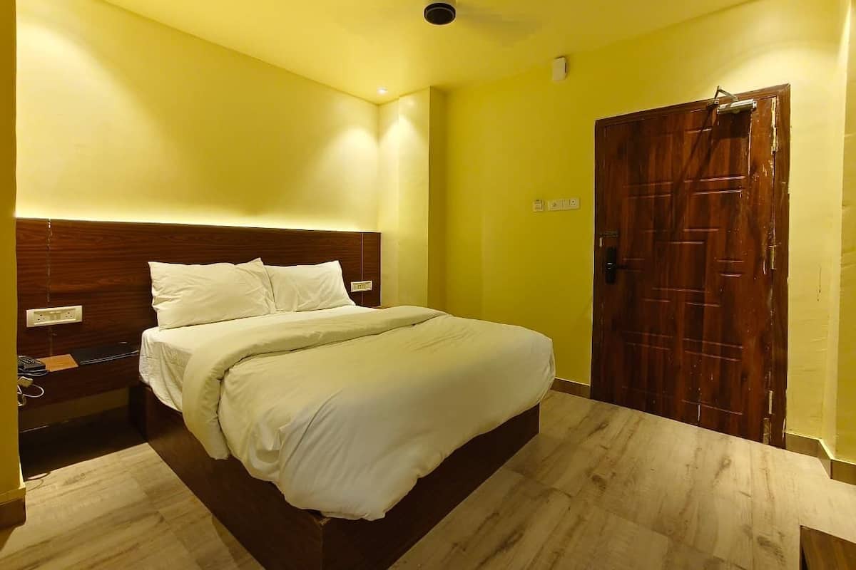 Quarto de hotel com cama, cabeceira de madeira, mesa de cabeceira, porta e ventilador de teto.