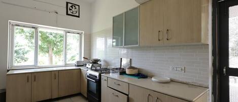 A kitchen with light wood cabinets, a stove, and a window with a view of trees.