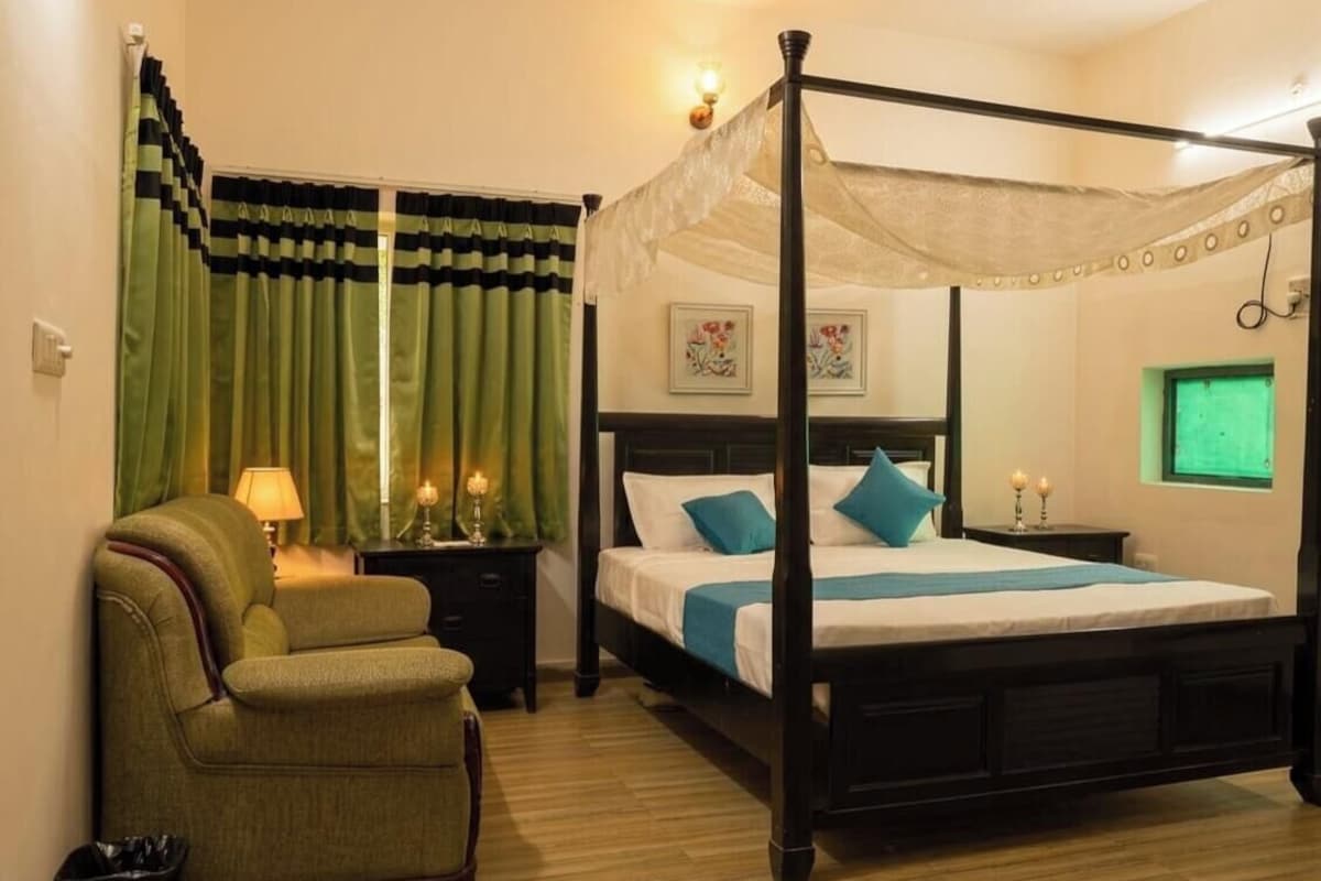 Una cama con dosel, un sillón verde, lámparas de noche y una obra de arte floral enmarcada en la pared.