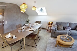 Ein modernes Wohnzimmer mit Essbereich, grauem Sofa und rundem Holztisch mit Getränken.