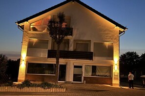 Ein zweistöckiges Haus mit Balkon, großen Fenstern und einem Baum im Vorgarten.