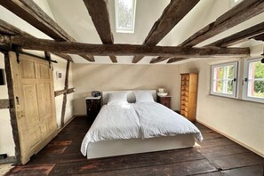 A bedroom with a wooden ceiling, a bed with white bedding, a nightstand, a wooden cabinet, and a window. - Holiday home with 2 bedrooms (Kottenheim)