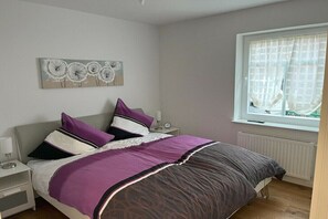 A bedroom with a bed, nightstands, a window with curtains, and a wall art piece. - Holiday apartment with 2 bedrooms (Norddeich)