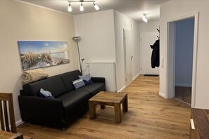 A modern living room with a black sofa, a wooden coffee table, a painting on the wall, and a radiator. - Holiday apartment with 2 bedrooms (Norddeich)