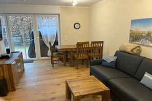 A living room with a wooden dining table, chairs, a black sofa, and a coffee table. - Holiday apartment with 2 bedrooms (Norddeich)