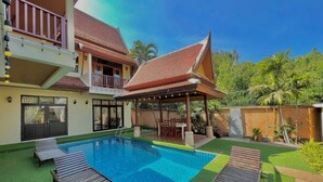 Ein Pool mit Liegestühlen, eine überdachte Sitzecke und ein zweistöckiges Gebäude mit Balkon.