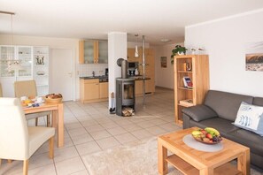Ein modernes Wohnzimmer mit einer Couch, einem Couchtisch mit Obst, einem Bücherregal und einer Küchenzeile mit Schränken und einem Herd.