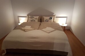 Ein ordentlich bezogenes Bett mit Kopfteil, zwei Nachttische mit Lampen und ein gefaltetes Handtuch auf dem Bett.