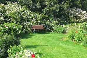 Ein Garten mit einer Bank, üppigem Grün und verschiedenen blühenden Pflanzen.