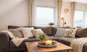 Ein gemütliches Wohnzimmer mit einer Couch, einem Couchtisch mit Kerzen und Meerblick durch große Fenster.