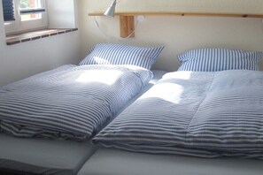 Ein Zimmer mit zwei Einzelbetten, einem Nachttisch, einer Lampe und einem Fenster mit Jalousien.