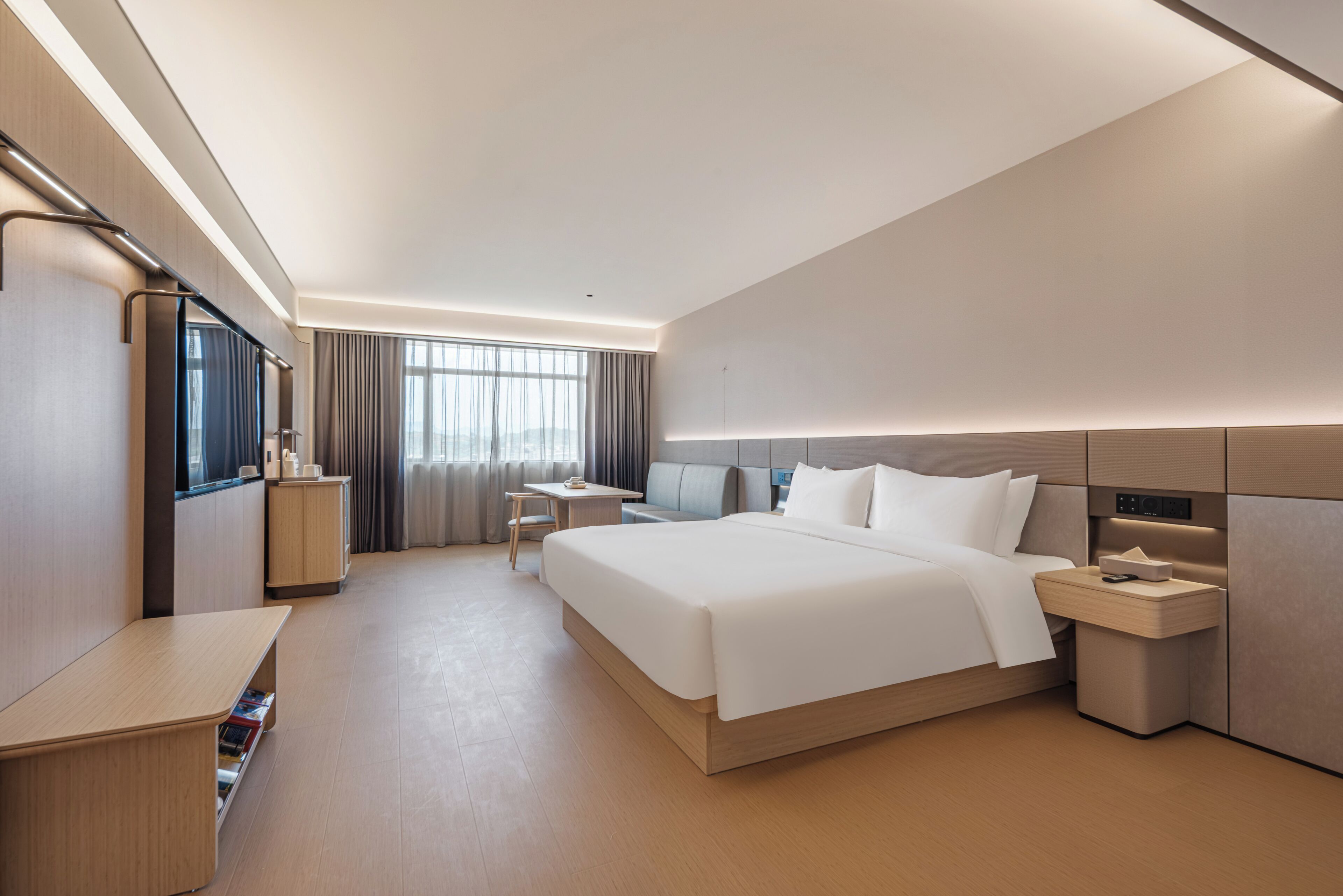 Una habitación de hotel moderna con una cama grande, mesitas de noche, un escritorio y vistas al exterior.