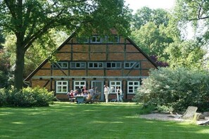 Ein traditionelles Gebäude mit einem steilen Satteldach, zahlreichen Fenstern und einem gepflegten Rasen mit Außenbestuhlung.