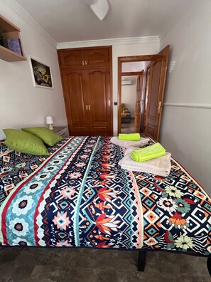 Une chambre à coucher avec une couvre-lit à motifs, un coussin vert, une serviette pliée et une armoire en bois.