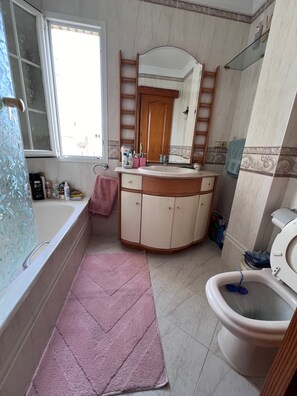Ein Badezimmer mit Badewanne, Waschbecken, Toilette, Spiegel und Fenster.