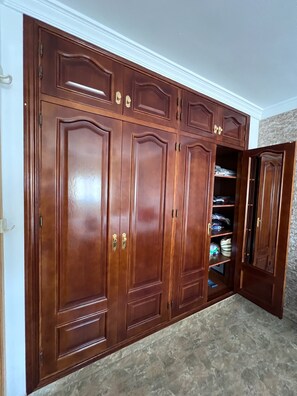 Ein großer, hölzerner Kleiderschrank mit mehreren Türen und Schubladen, eine Steinwand und ein gefliester Boden.