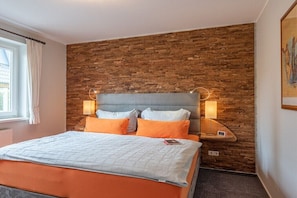 Ein Schlafzimmer mit Ziegelwand, einem Bett mit orangefarbener Bettwäsche, zwei Nachttischlampen und einem Fenster mit Vorhängen.