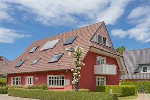 Ein rotes Gebäude mit zahlreichen Fenstern, einem Balkon und einem gepflegten Garten.
