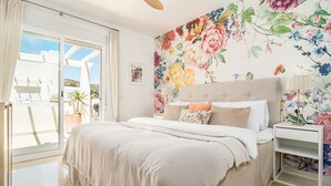 A bedroom with a bed, a nightstand, a window with curtains, and a floral wall mural. - Bv373a - Corner Penthouse With Rooftop Terrace (Mijas)