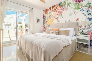 Une chambre à coucher avec un lit, une table de chevet, une fenêtre avec des rideaux et une décoration murale à motifs floraux.