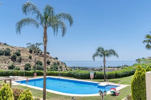En swimmingpool med utsikt över havet, omgiven av palmer och ett kuperat landskap.