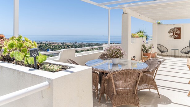 A terrace with wicker furniture, a table, potted plants, and a view of the sea. - Bv373a - Corner Penthouse With Rooftop Terrace (Mijas)