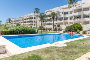 Une piscine équipée d’une bouée de sauvetage, entourée d’une pelouse et de palmiers, avec un immeuble à plusieurs étages en arrière-plan.