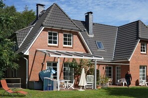 Ein Backsteinhaus mit überdachter Terrasse, Schornstein und einer Person, die vorbeigeht.