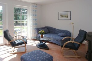 Ein Wohnzimmer mit einer Couch, zwei Sesseln, einem Glastisch und einem Kamin.