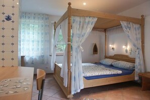 Ein Himmelbett mit Baldachin, ein Holztisch mit Stühlen und ein Fenster mit Vorhängen.