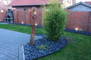 Ein Backsteinhaus mit rotem Dach, einem Steinkamin und einem Garten mit Baum und Kiesweg.