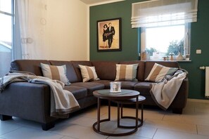 Ein Wohnzimmer mit einem braunen Ecksofa, einem kleinen runden Tisch und einem gerahmten Bild an der Wand.