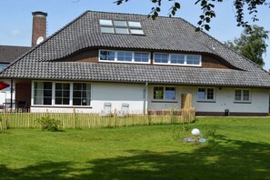 Ein zweigeschossiges Haus mit Ziegeldach, Schornstein und umzäunter Garten.